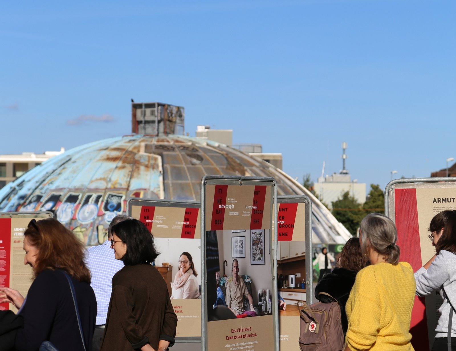 DSI OIS People standing and looking at outdoor display boards with a weathered, dome-shaped structure in the background under a clear blue sky. Designed by Circular Design, a not-for-profit web design agency.